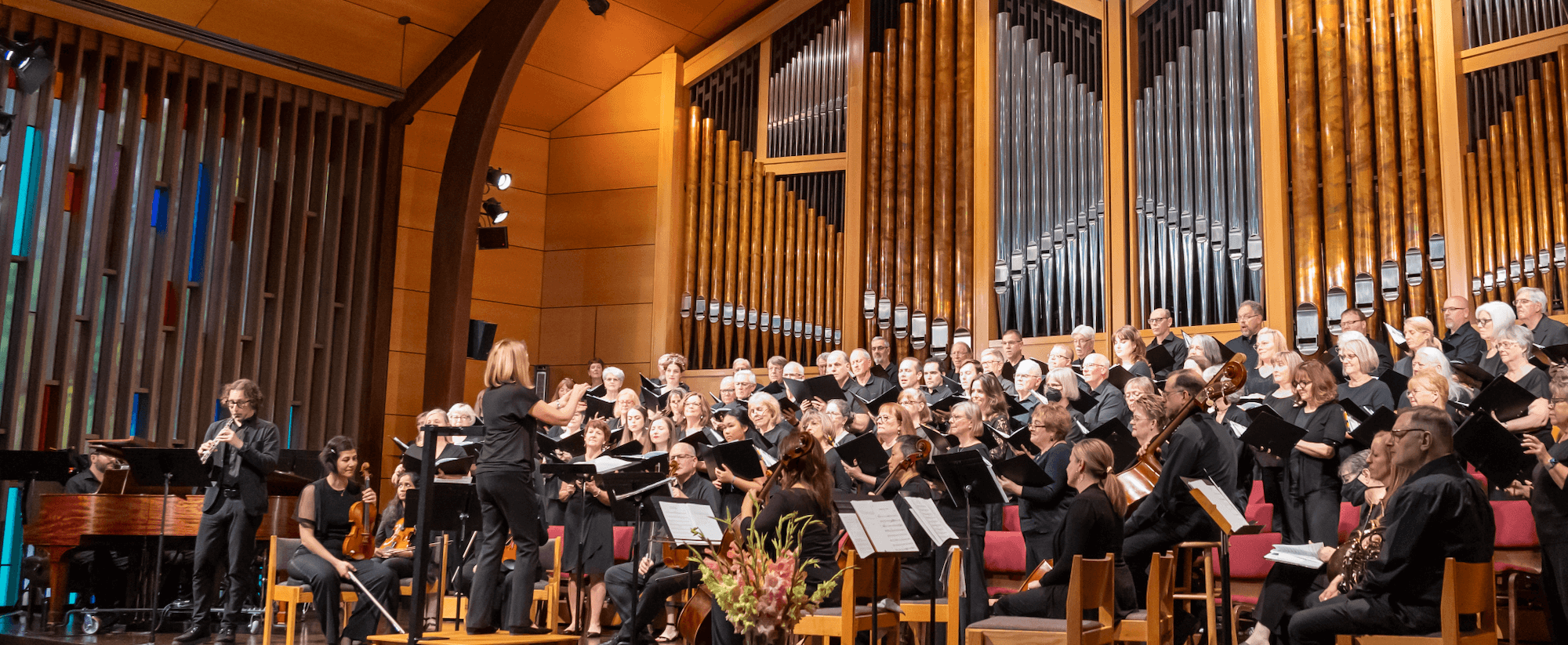 a choir and orchestra on stage with organ pipes in the background